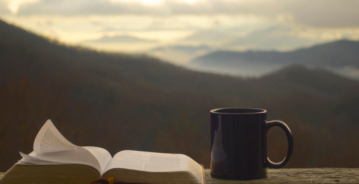 Coffee and the Bible on a rail in front of the mountains