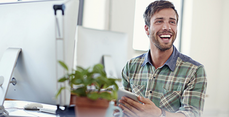 Young man smiling while working on computer and tablet